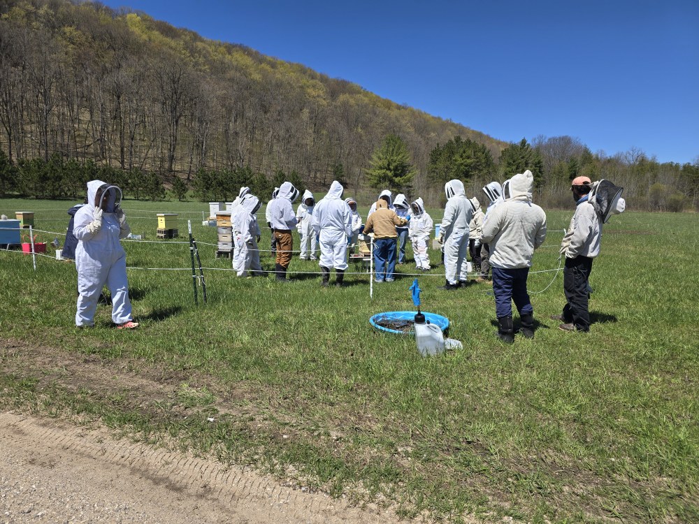 Beekeeper Rick Dimanin wearing a brown coat teaching his students during the beekeeping classes at the class apiary.